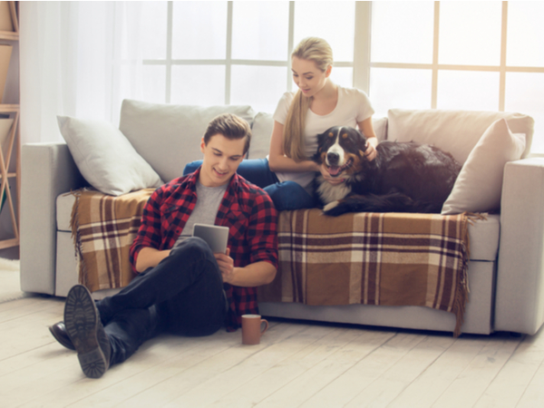 Man holding the tablet and a girl sitting on the couch with a dog