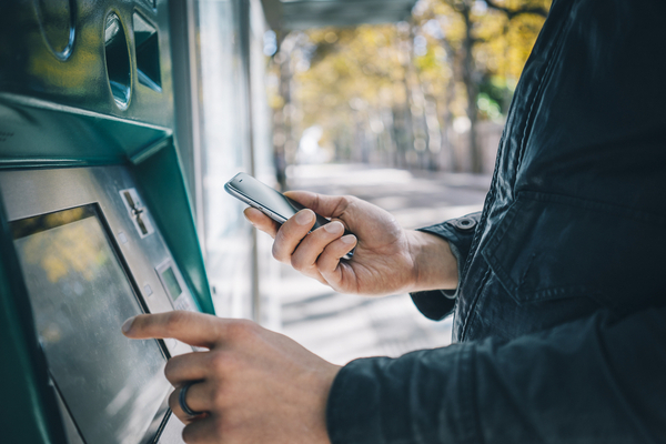 Male hands using smart phone while typing on ATM