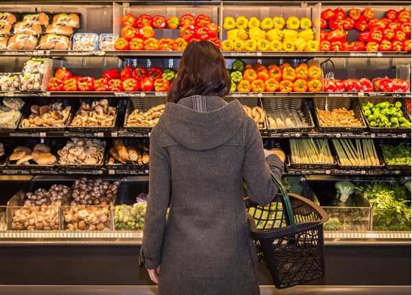 Su - Woman standing in front of a row of produce in a grocery store Woman standing in front of a row of produce in a grocery store