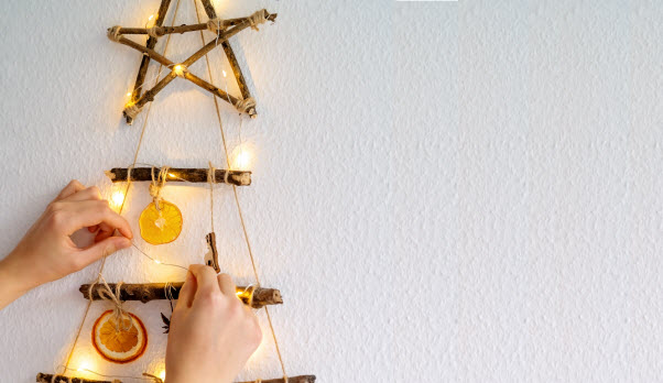 StepUp - Solar lights or battery powered for Christmas hands of a woman decorating handmade craft Christmas tree made with natural materials and lights hanging on wall