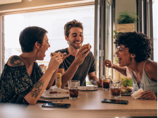 Cheerful young people eating burger and enjoying at a restaurant.