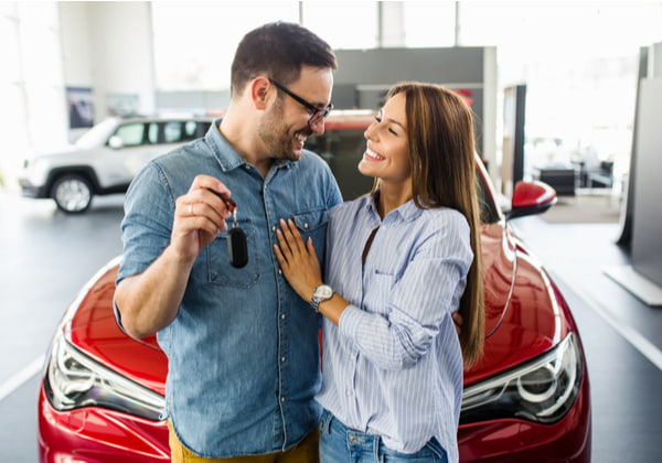 Beautiful young smiling couple holding a key of their new car