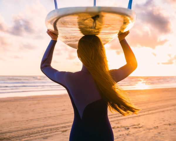 Woman with surfboard on a beach at sunset