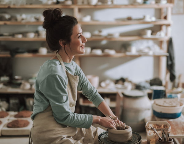 Beautiful craftswoman making clay bowl in pottery workshop