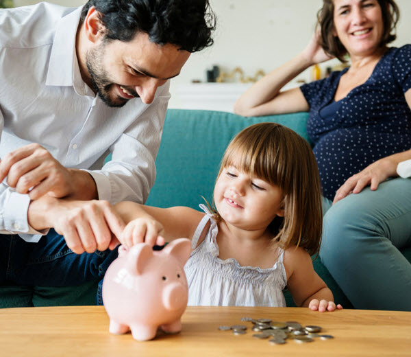 Father helping daughter to put coins in piggy bank