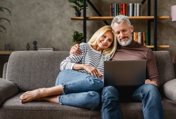 Senior couple using laptop and smiling while resting on couch
