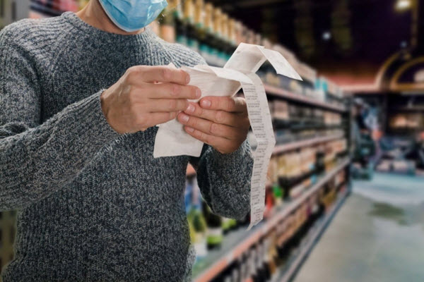 Male customer doing grocery shopping at supermarket and feeling confused by bill