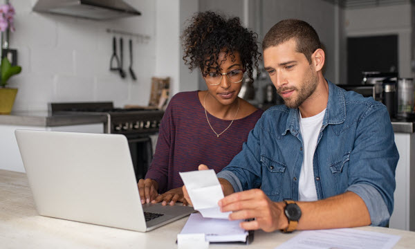 Step Up Group - Split your budget Young multiethnic couple checking bills while managing accounts on home banking app.