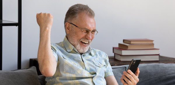 Step Up - Land tax law dropped Happy excited grandfather holding smartphone while sitting on the couch