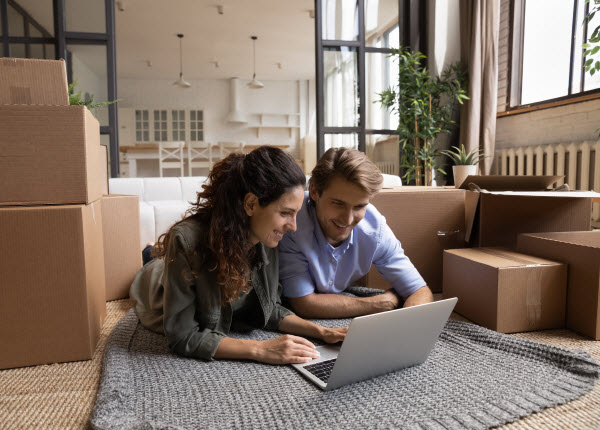 Couple happily checking laptop while on the floor with lots of boxes in their new home