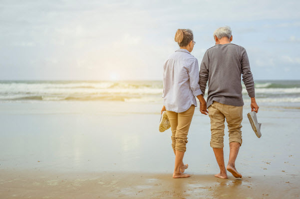 Senior couple walking on the beach holding hands at sunrise,