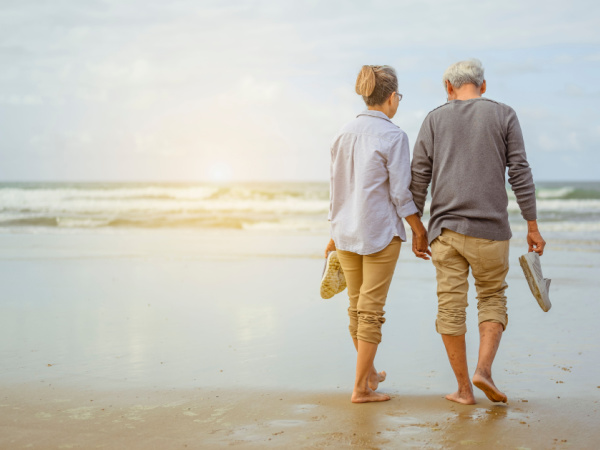 Senior couple walking on the beach holding hands at sunrise